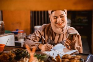 wanita berjualan makanan sambil menulis pemasukan